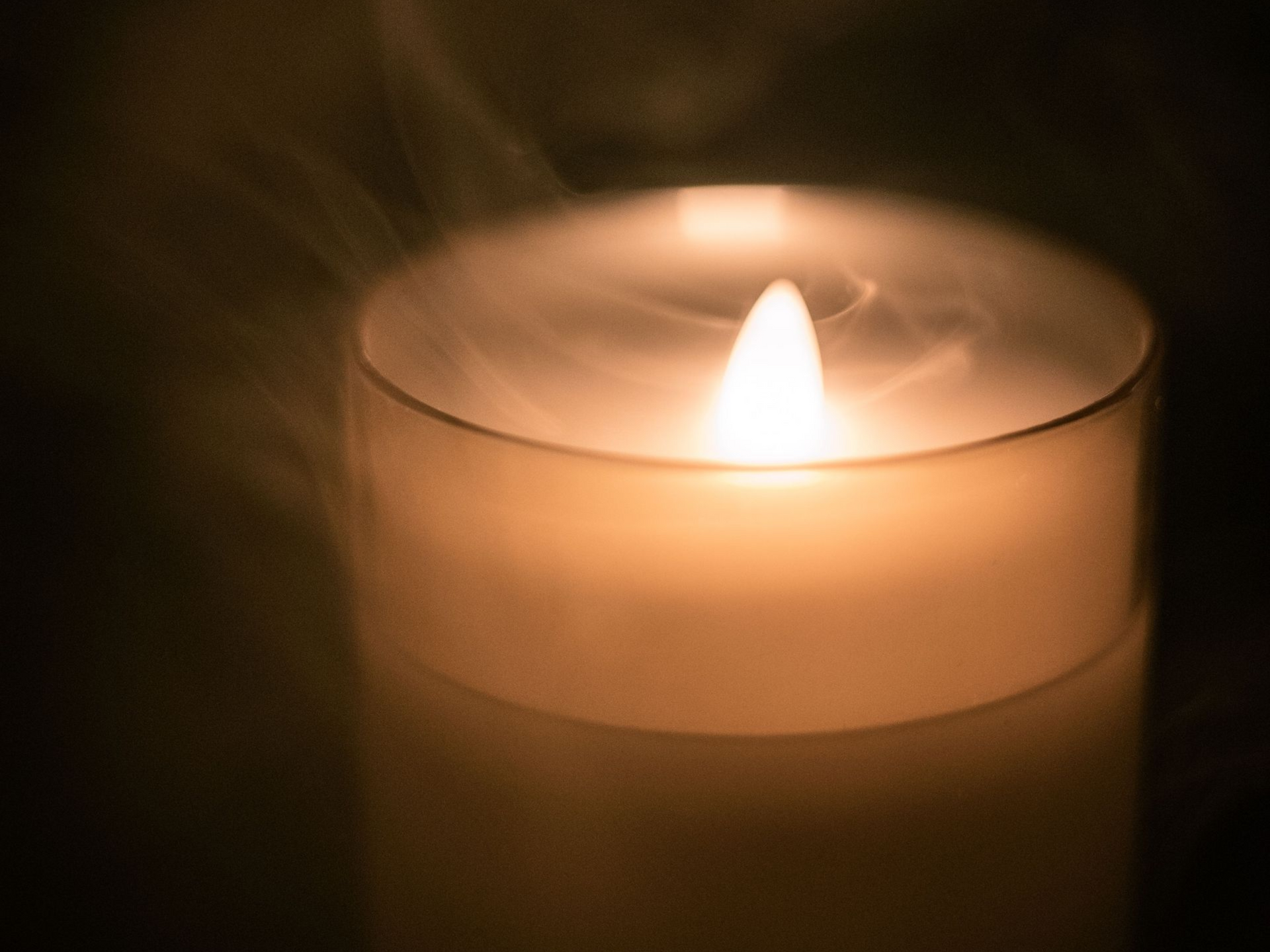 Une bougie blanche allumée brille dans un bougeoir en verre, dans une pièce faiblement éclairée.