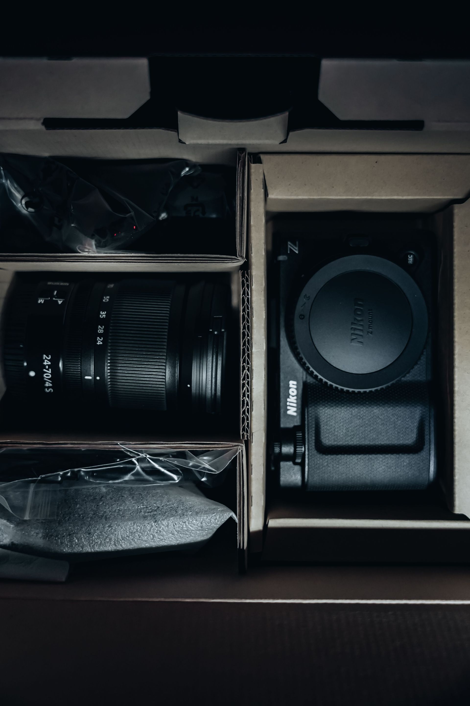 Kit d'appareil photo ouvert dans une boîte contenant un objectif, un boîtier et des accessoires rangés dans des compartiments.