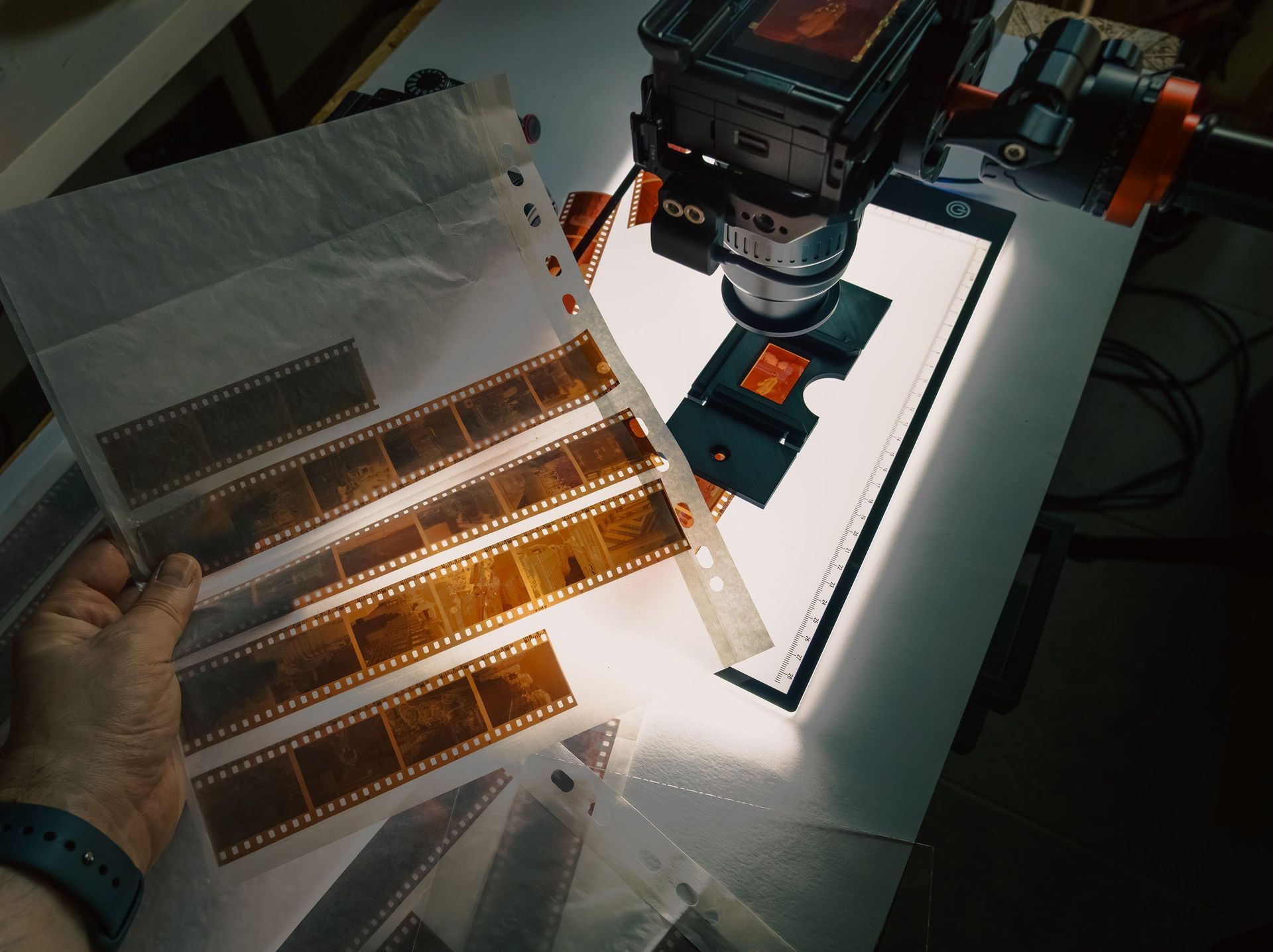 Main tenant des négatifs de film au-dessus d'un scanner de films éclairé par une rampe lumineuse orange