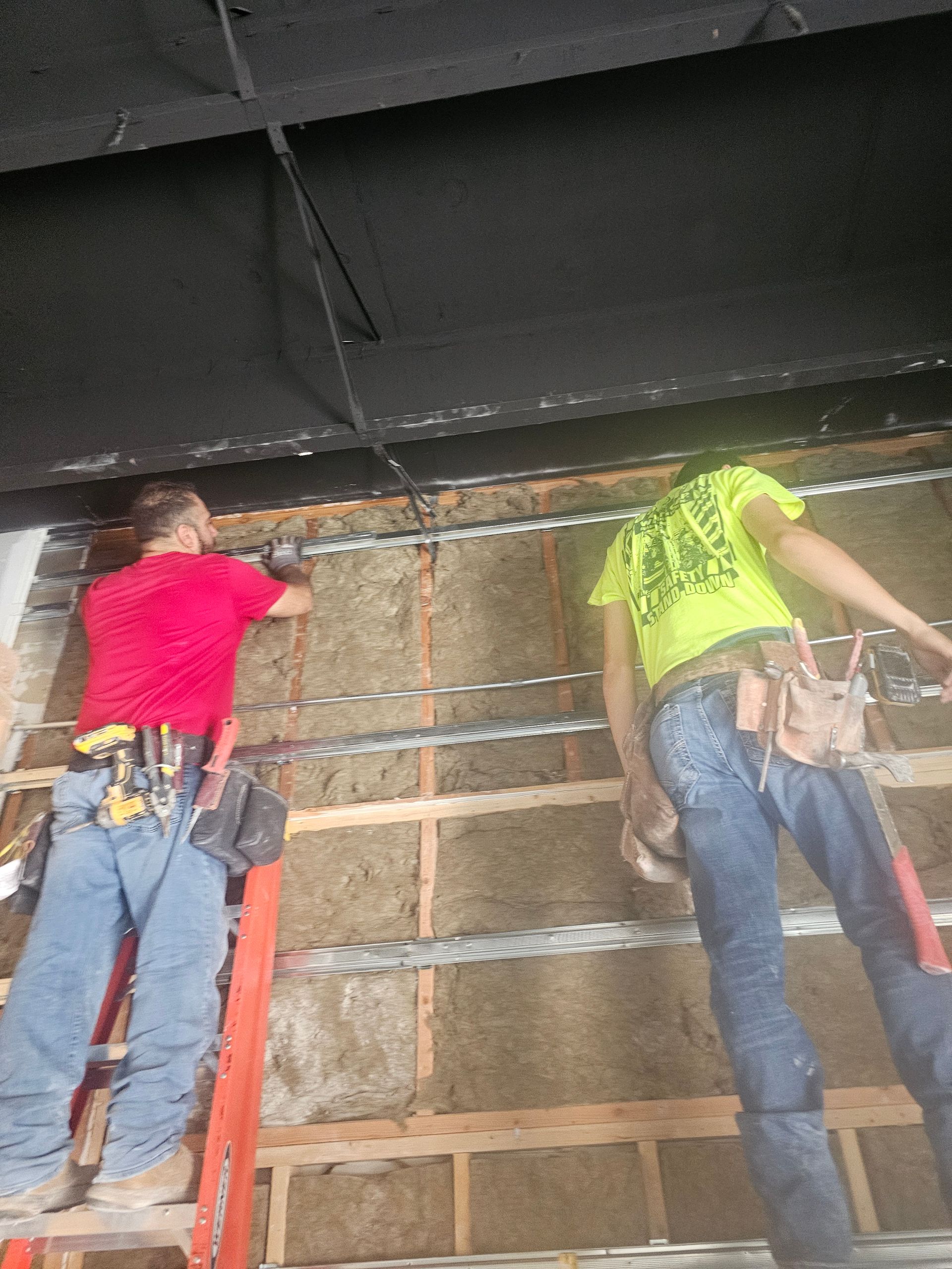 Two men are working on a wall on a ladder.