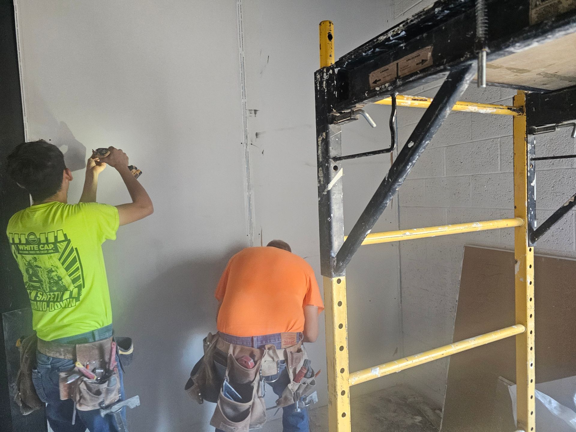 Two men are working on a wall next to a scaffolding.