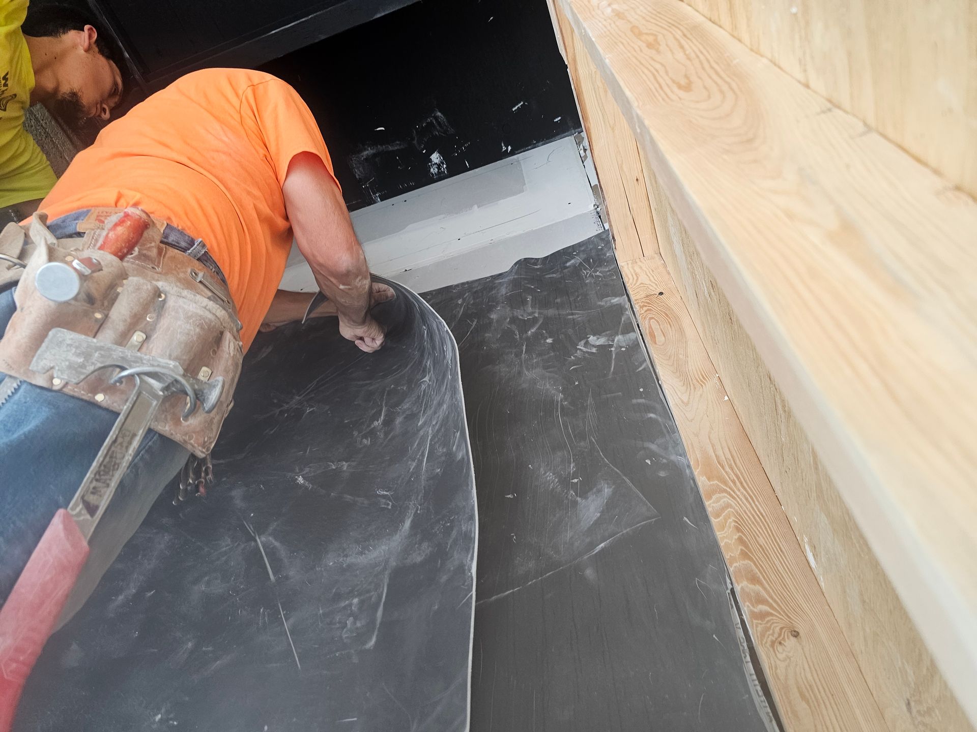 A man in an orange shirt is working on a tile floor