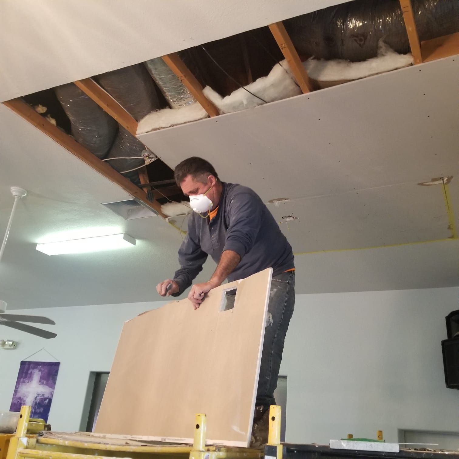 A man wearing a mask is working on a ceiling