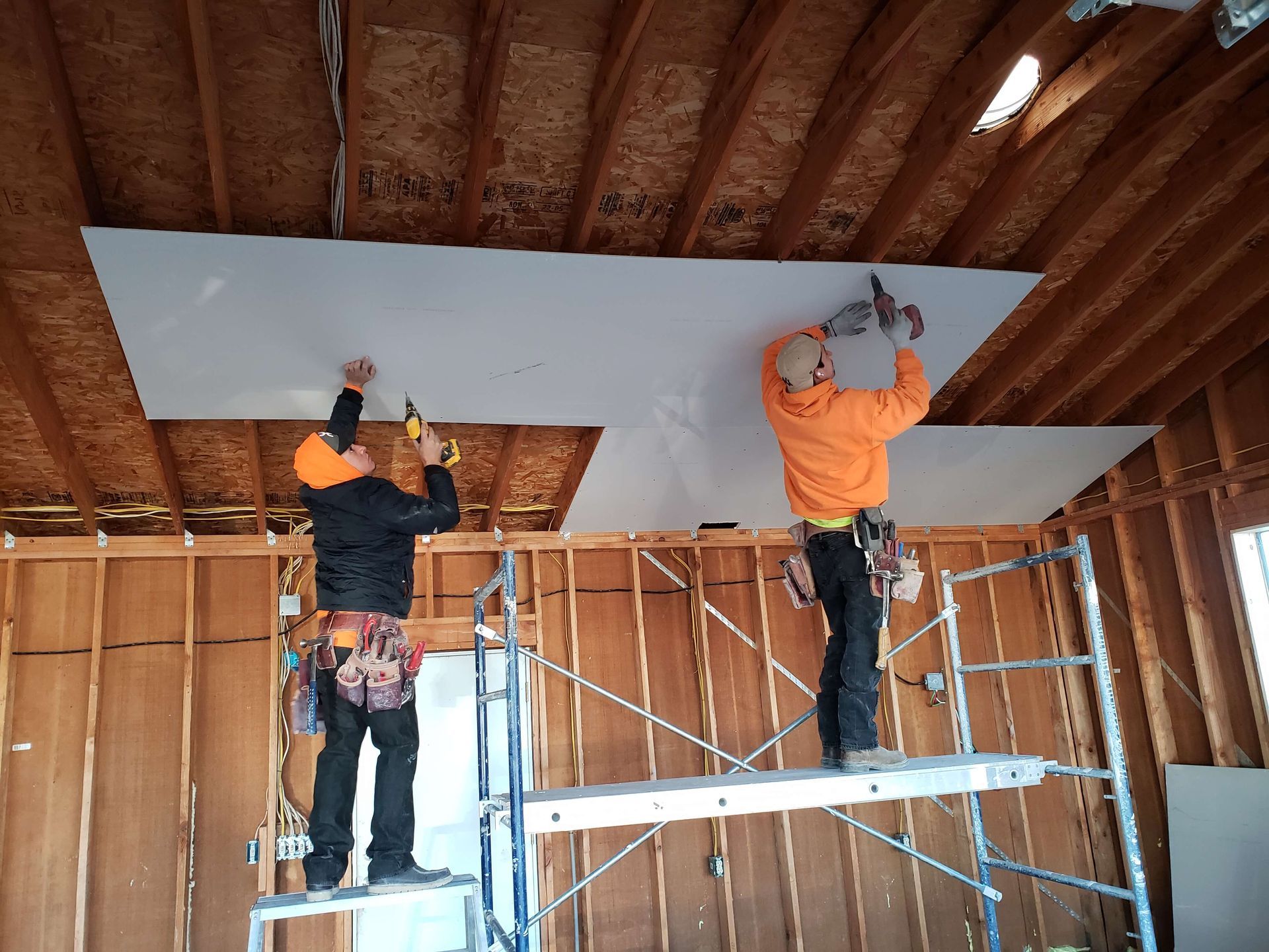 Two men are working on a ceiling while standing on a ladder.