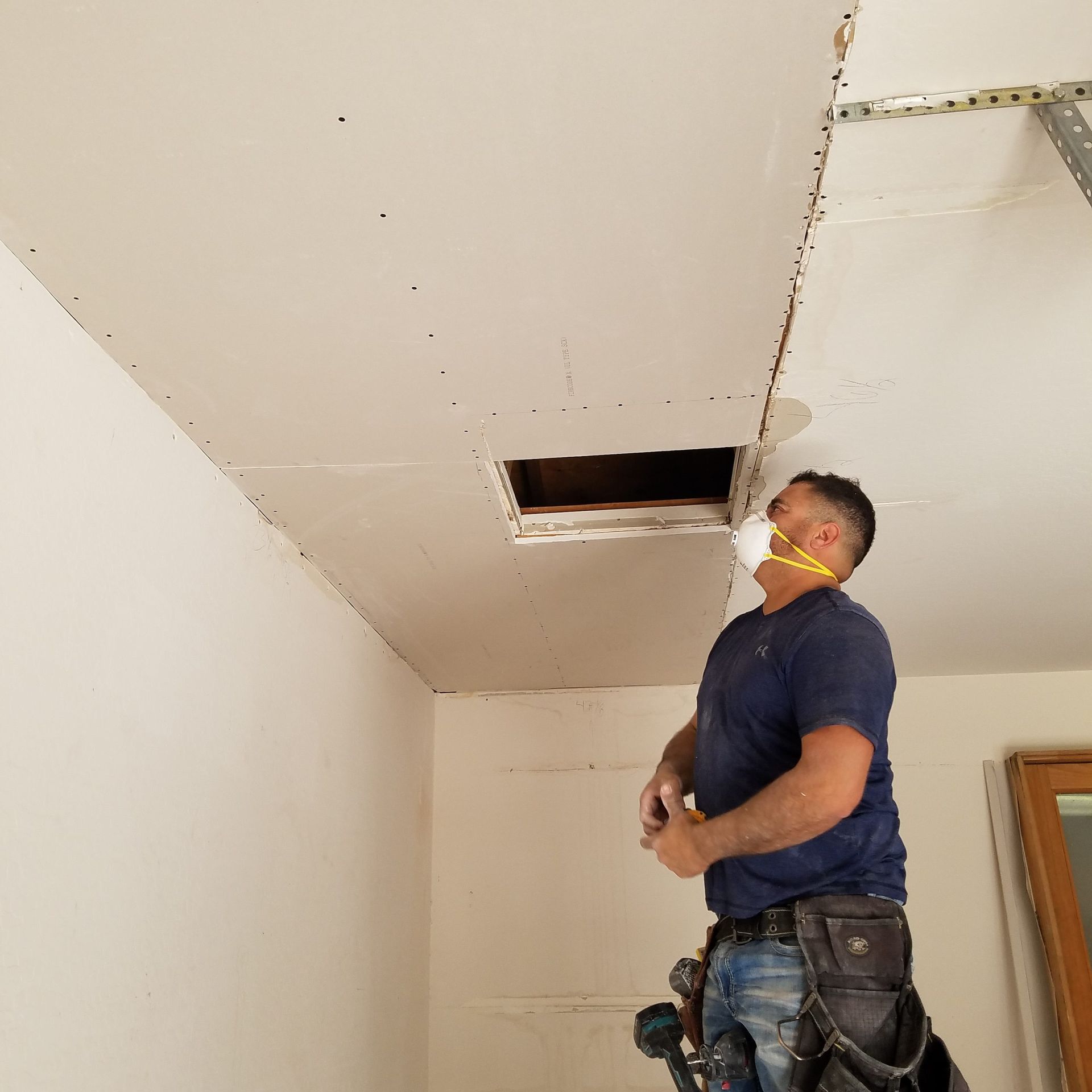 A man wearing a mask is working on a ceiling.
