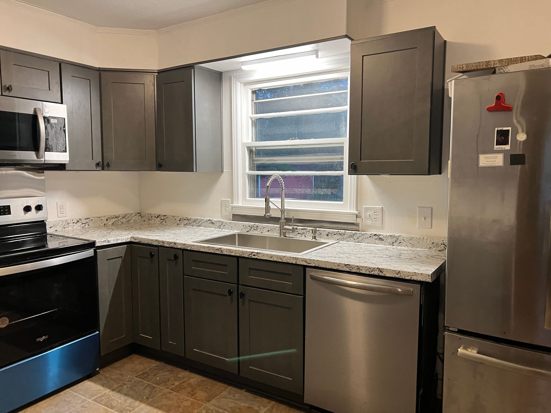 A kitchen with gray cabinets , stainless steel appliances , a sink , and a refrigerator.