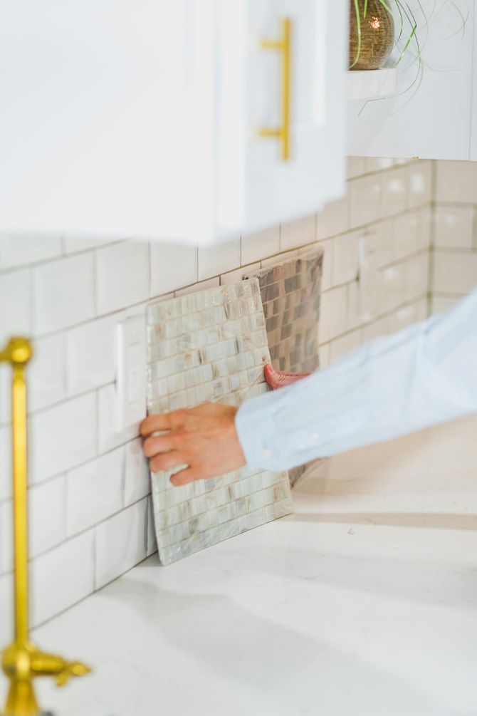 A person is holding a piece of tile on a kitchen wall.