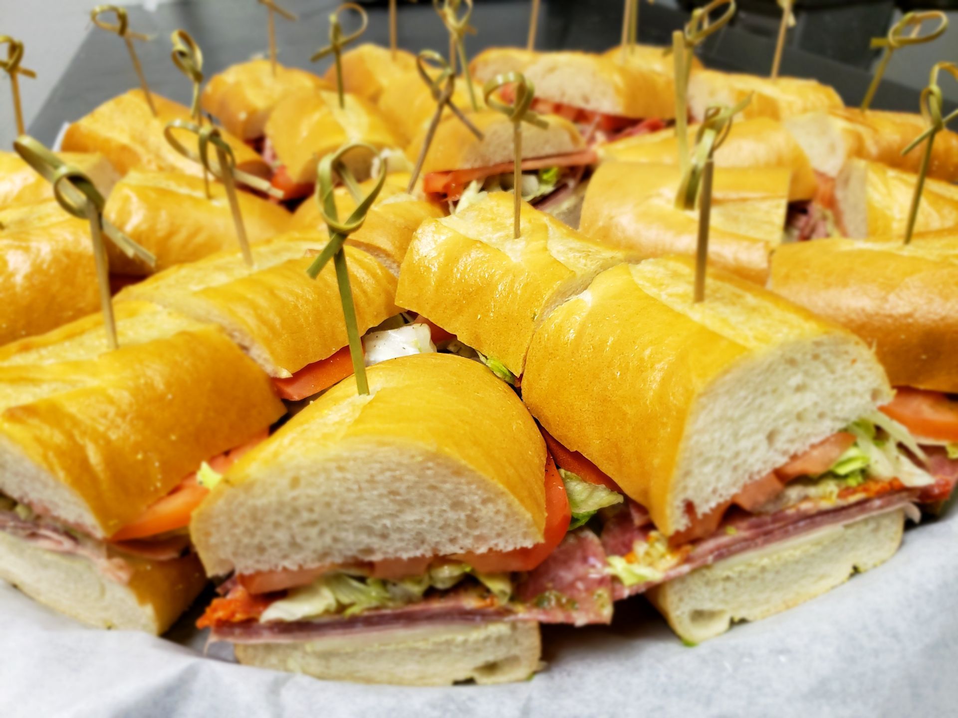 Tray of sliced baguette sandwiches with wooden skewers.