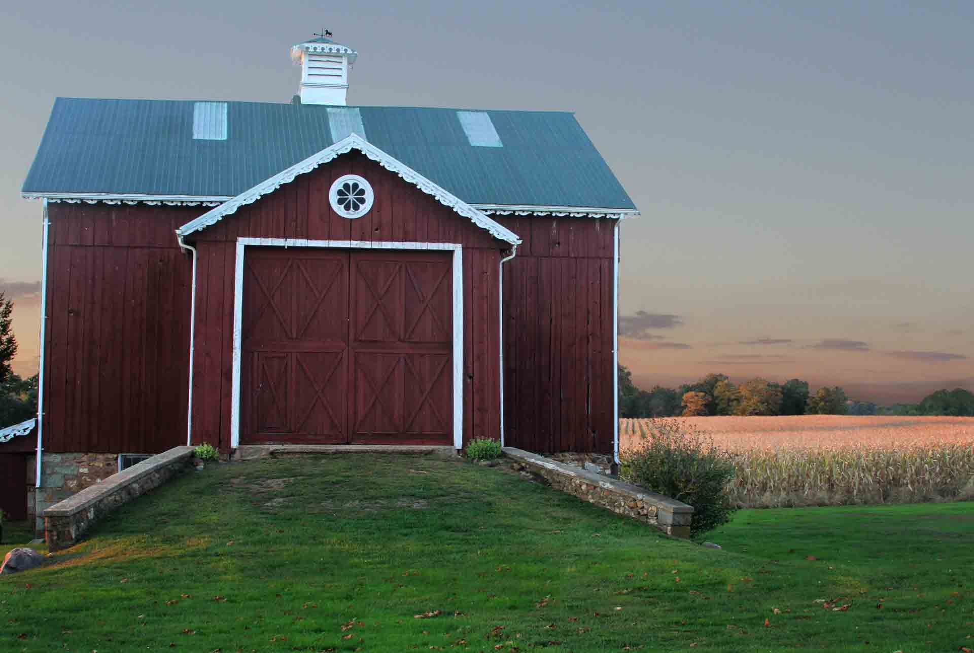 A red barn with a green roof is in the middle of a grassy field. barn door Smart Garage Door Service