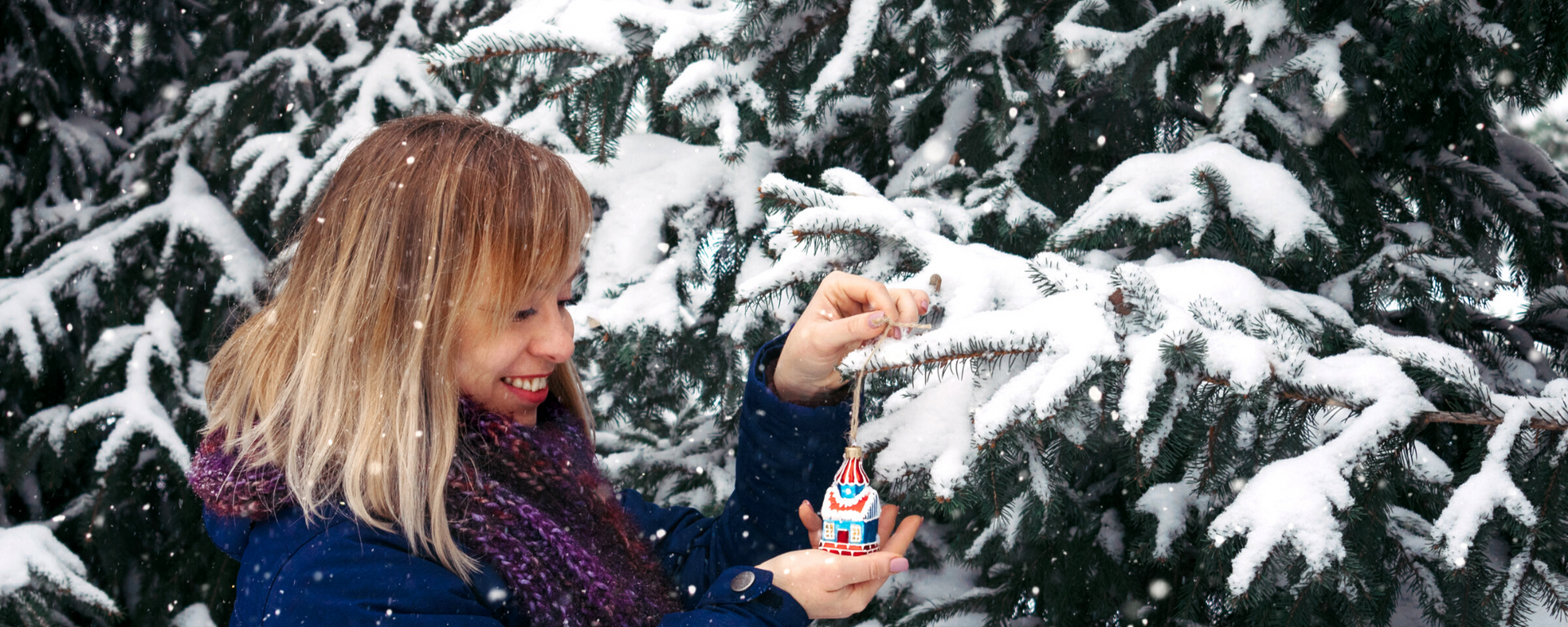 Woman adding an ornament to an outdoor Christmas tree