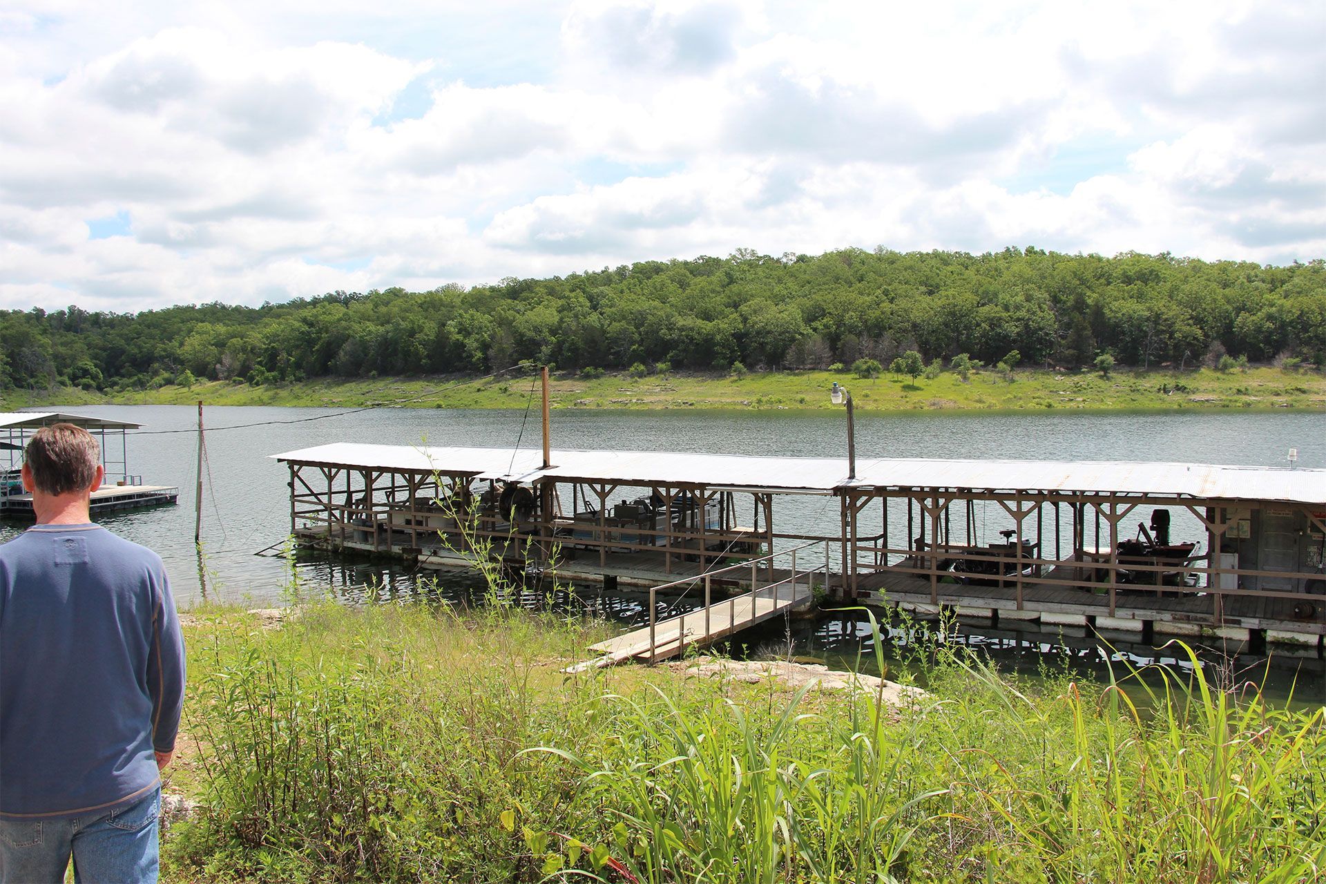 A man is standing on the shore of a lake looking at a dock.