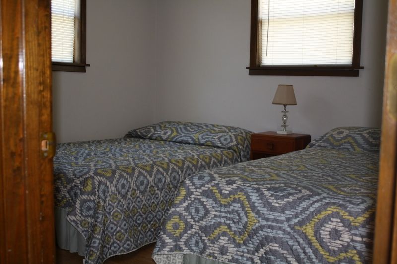 A bedroom with two twin beds , a nightstand , a lamp and two windows.