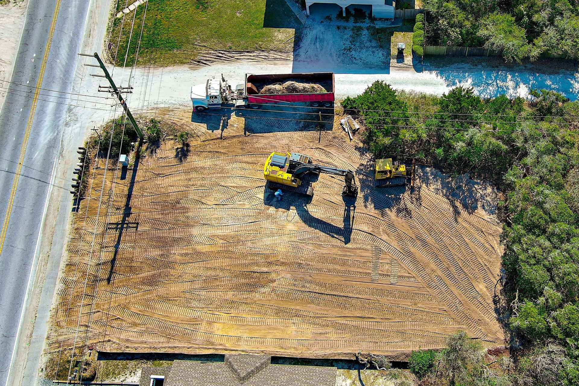 Aerial view of construction site with equipment: excavator, dump truck, and cleared land.