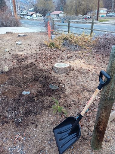 A shovel is leaning against a wooden post in the dirt.