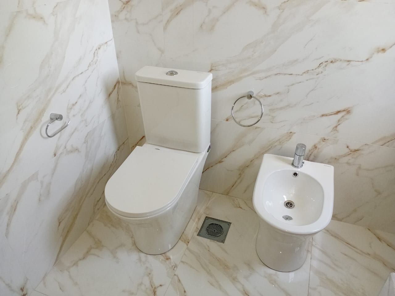 Inodoro y bidet en baño con paredes revestidas de mármol.