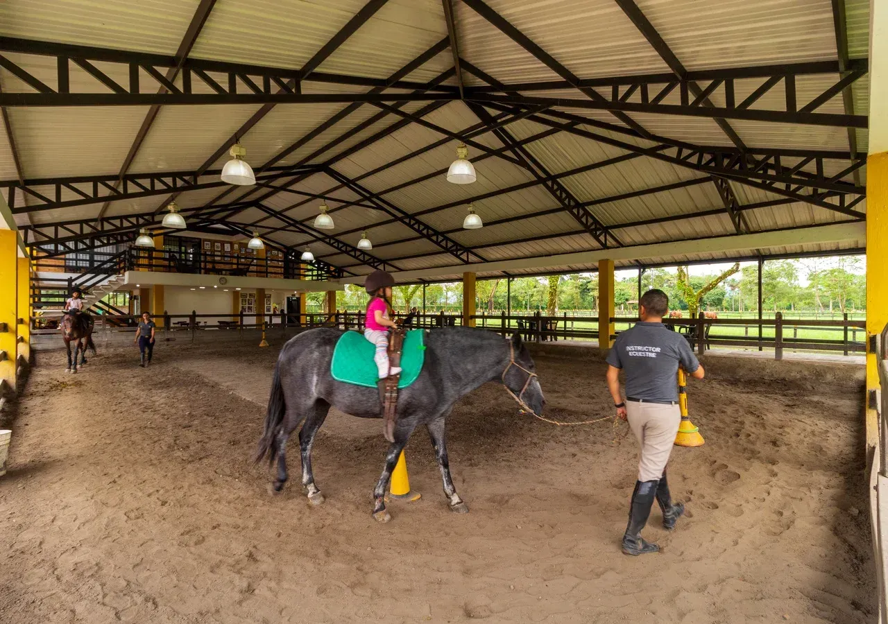 Niña cabalgando y siendo ayudada por el personal del Hotel Campestre La Potra, una experiencia familiar en Villavicencio.
