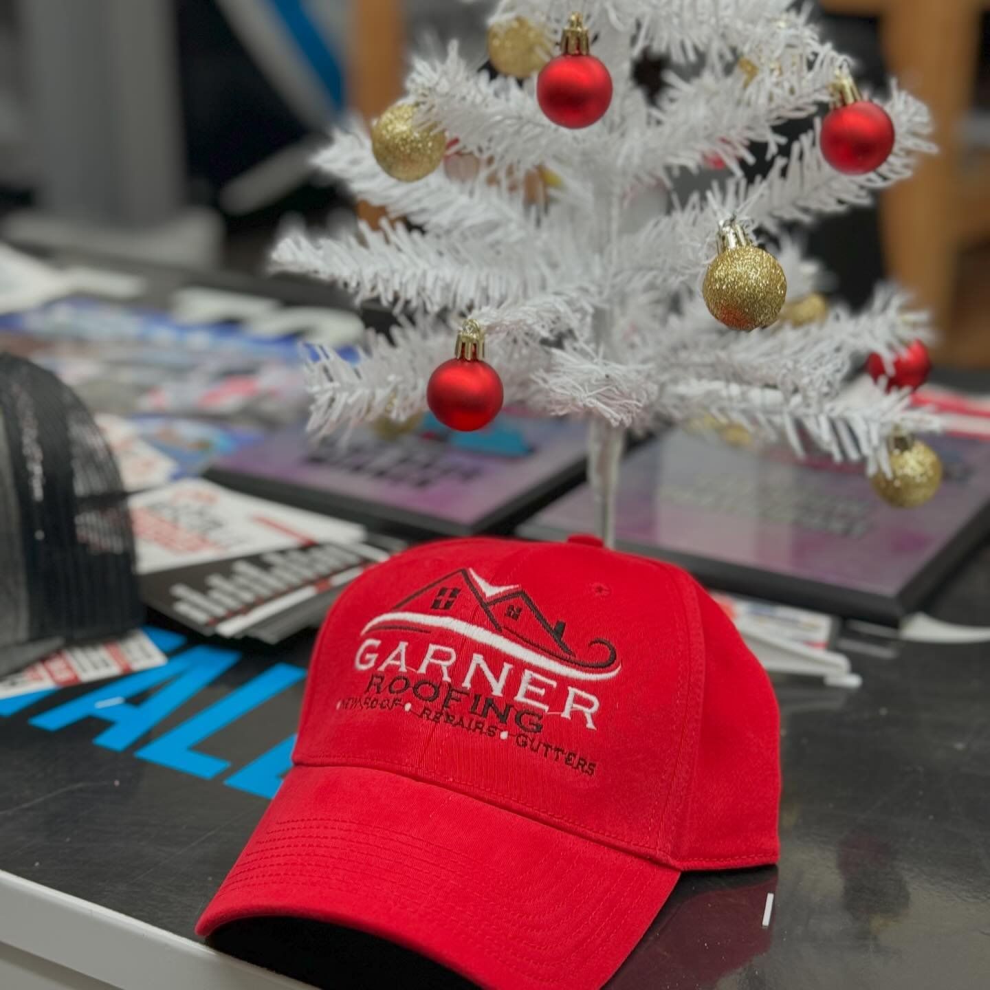 a red garner roofing hat sits in front of a small white christmas tree