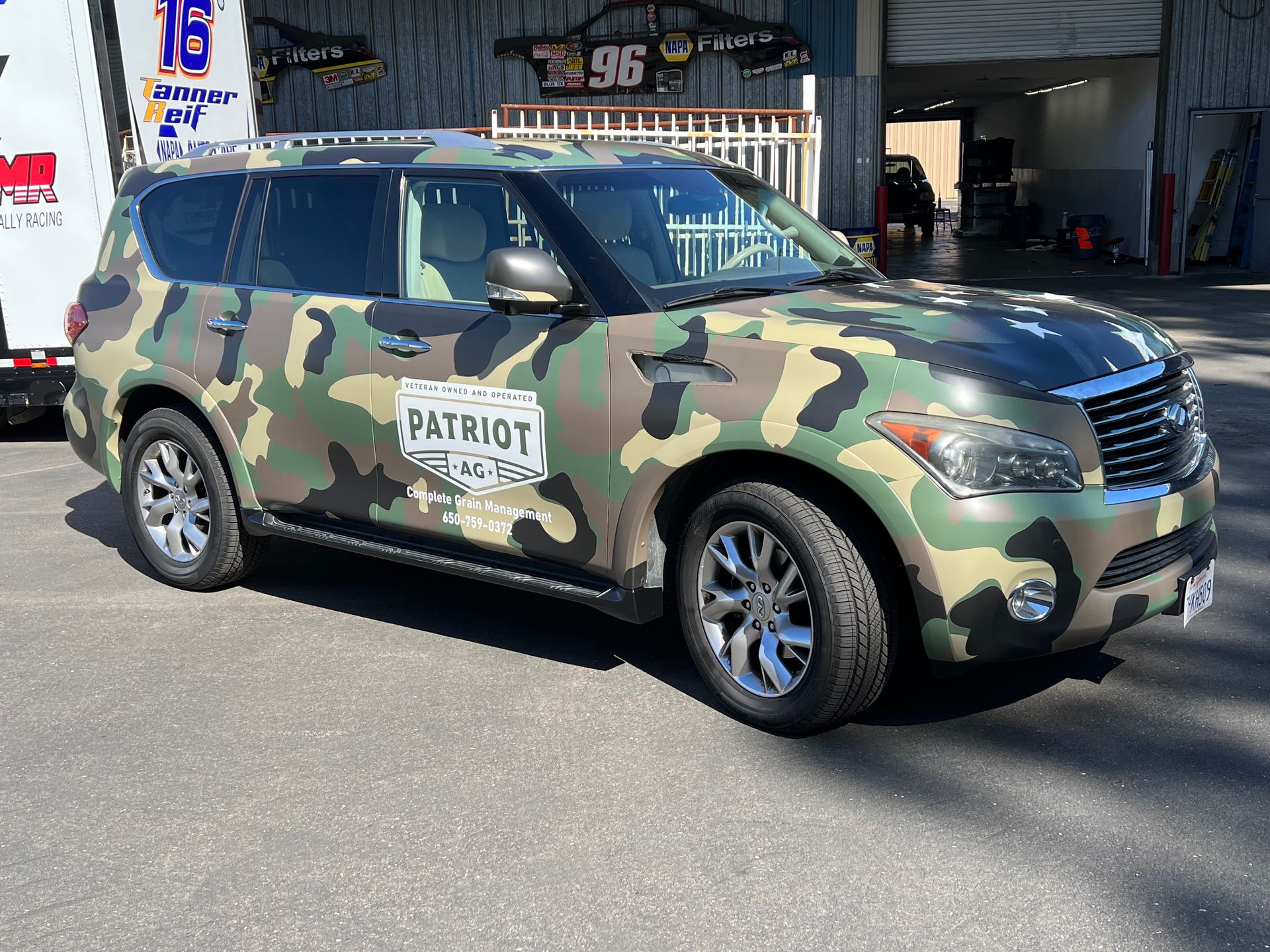 a car with a camouflage wrap is parked in front of a building .