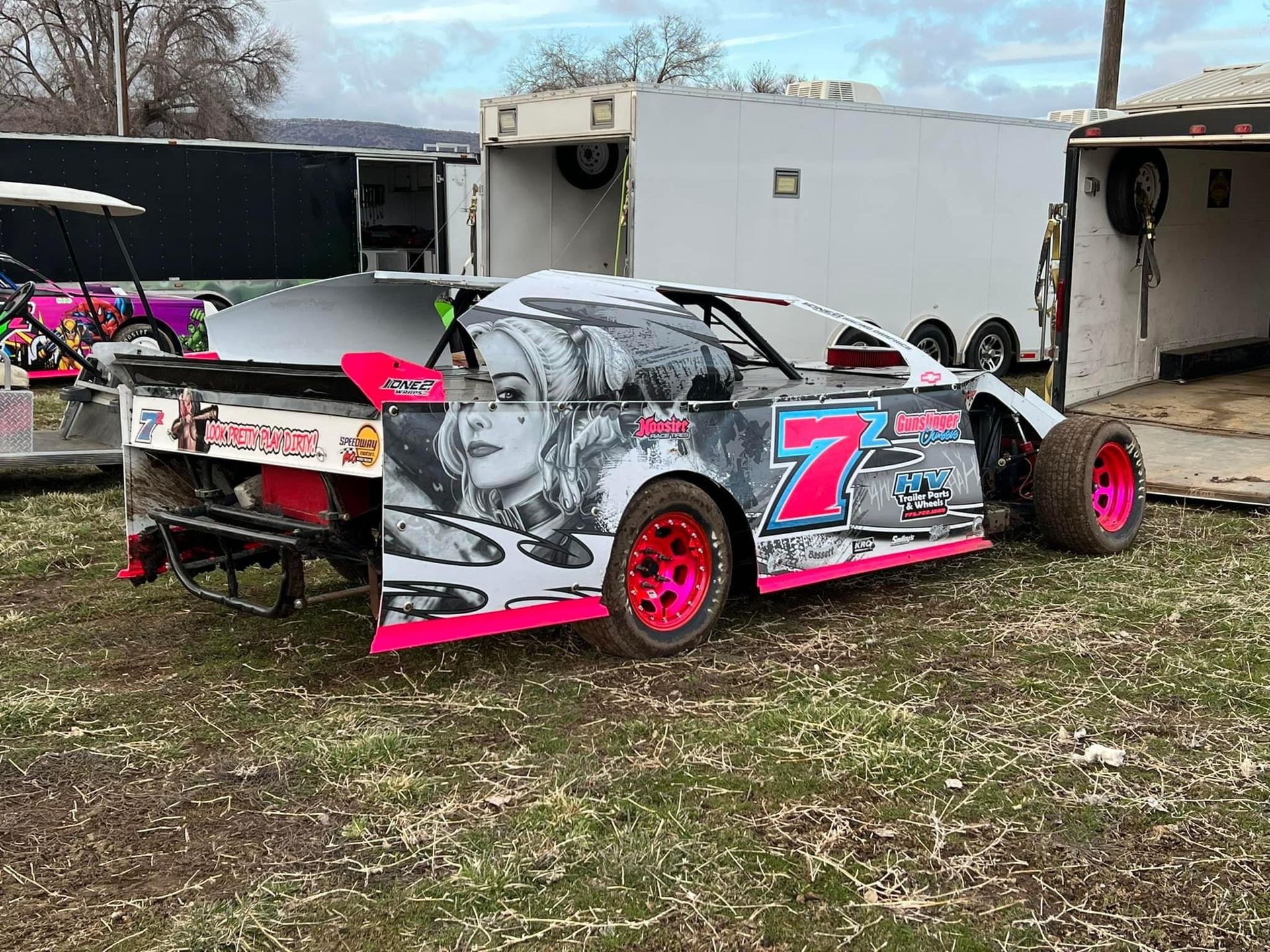 a race car is parked in a field next to a trailer .