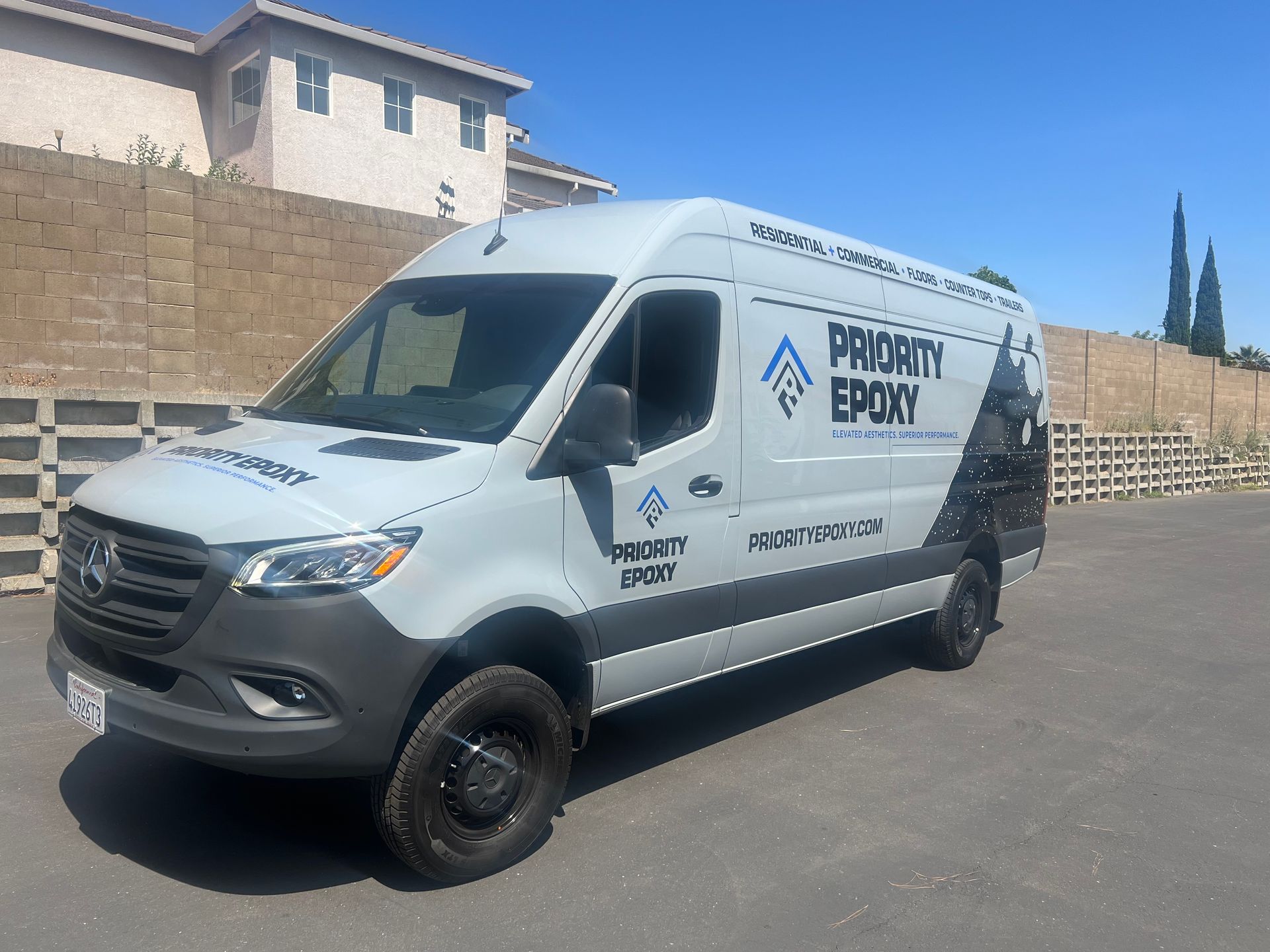 a white van with priority epoxy written on the side is parked in a parking lot .