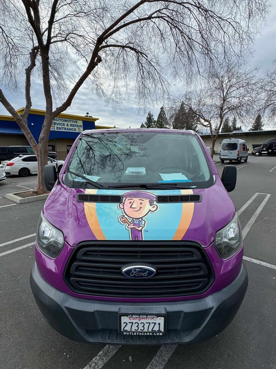 a purple van with a cartoon character on the front is parked in a parking lot .