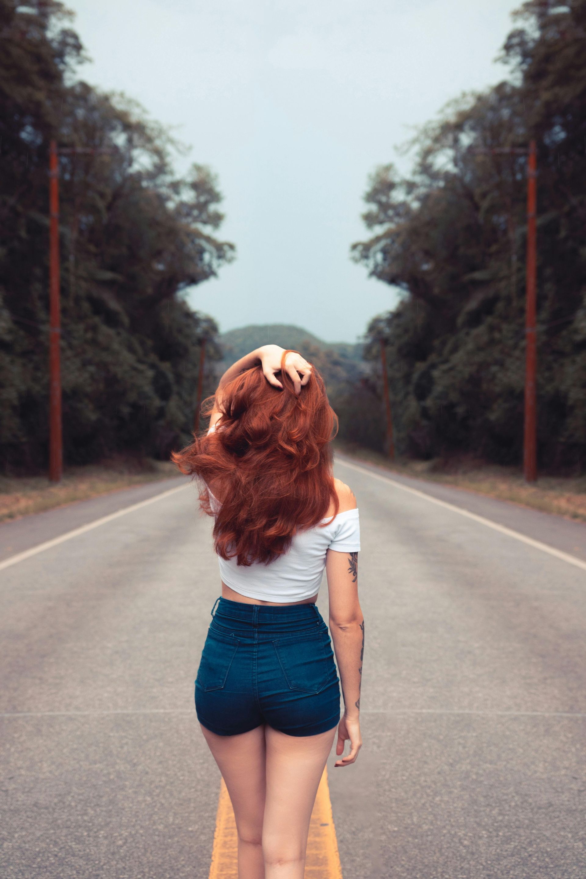 mujer pelirroja caminando en medio de una carretera en el bosque