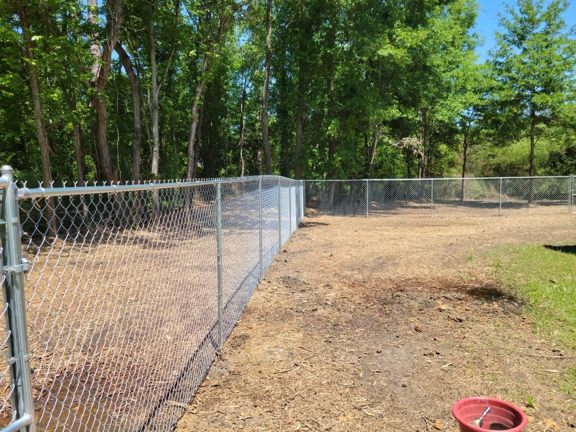A chain link fence surrounds a dog park with trees in the background.