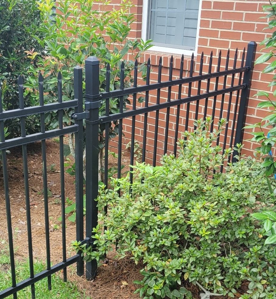 A black metal fence surrounds a bush in front of a brick building.