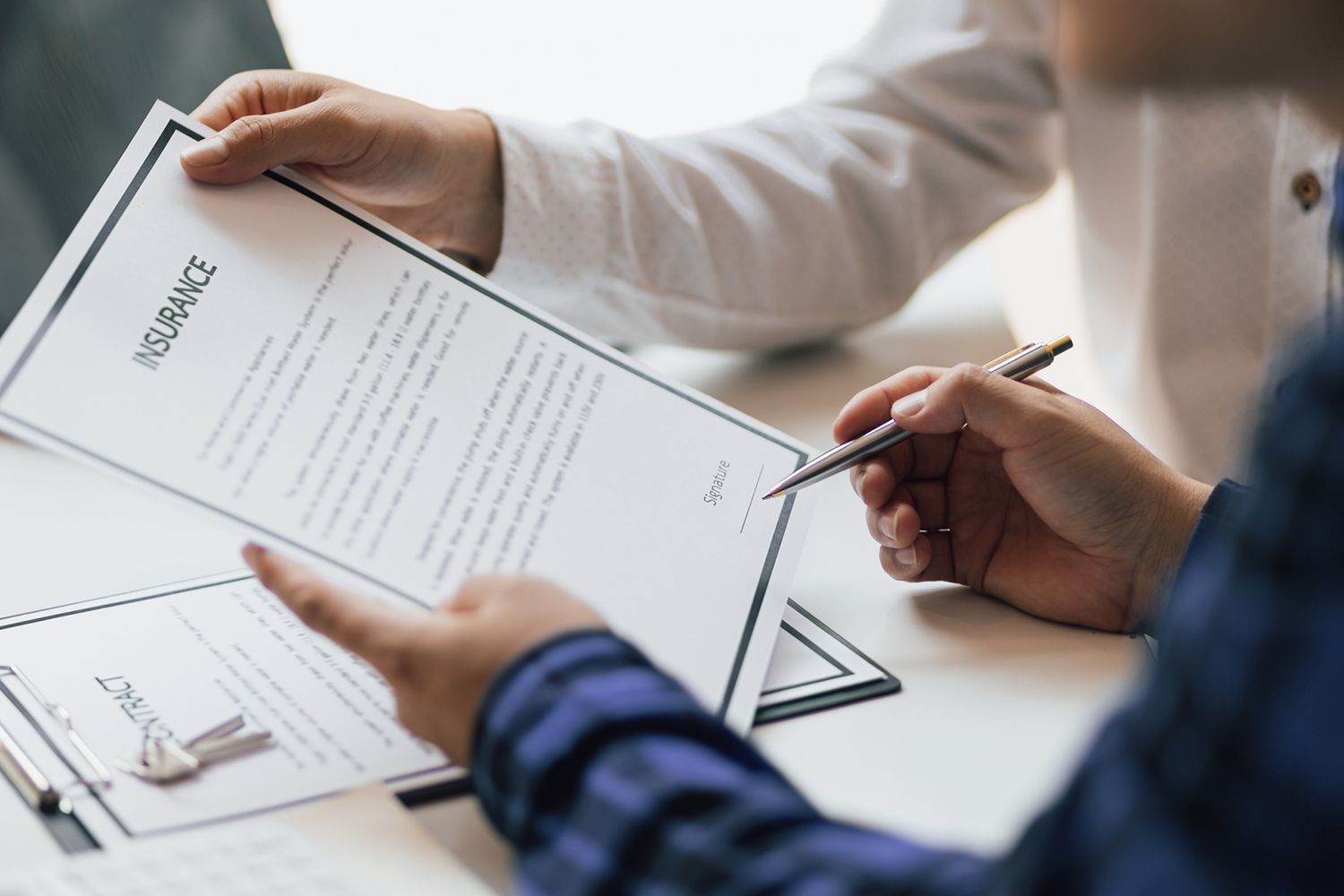 Hands signing an insurance document on a desk, possibly a business setting.