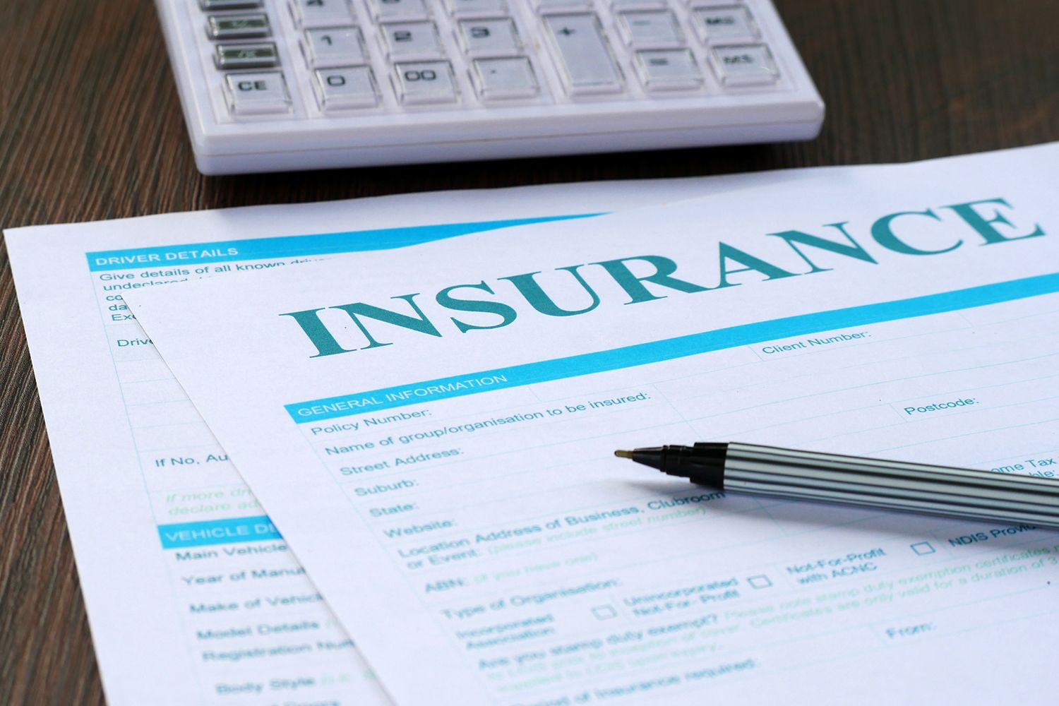 Insurance paperwork with a pen and calculator on a wooden table.