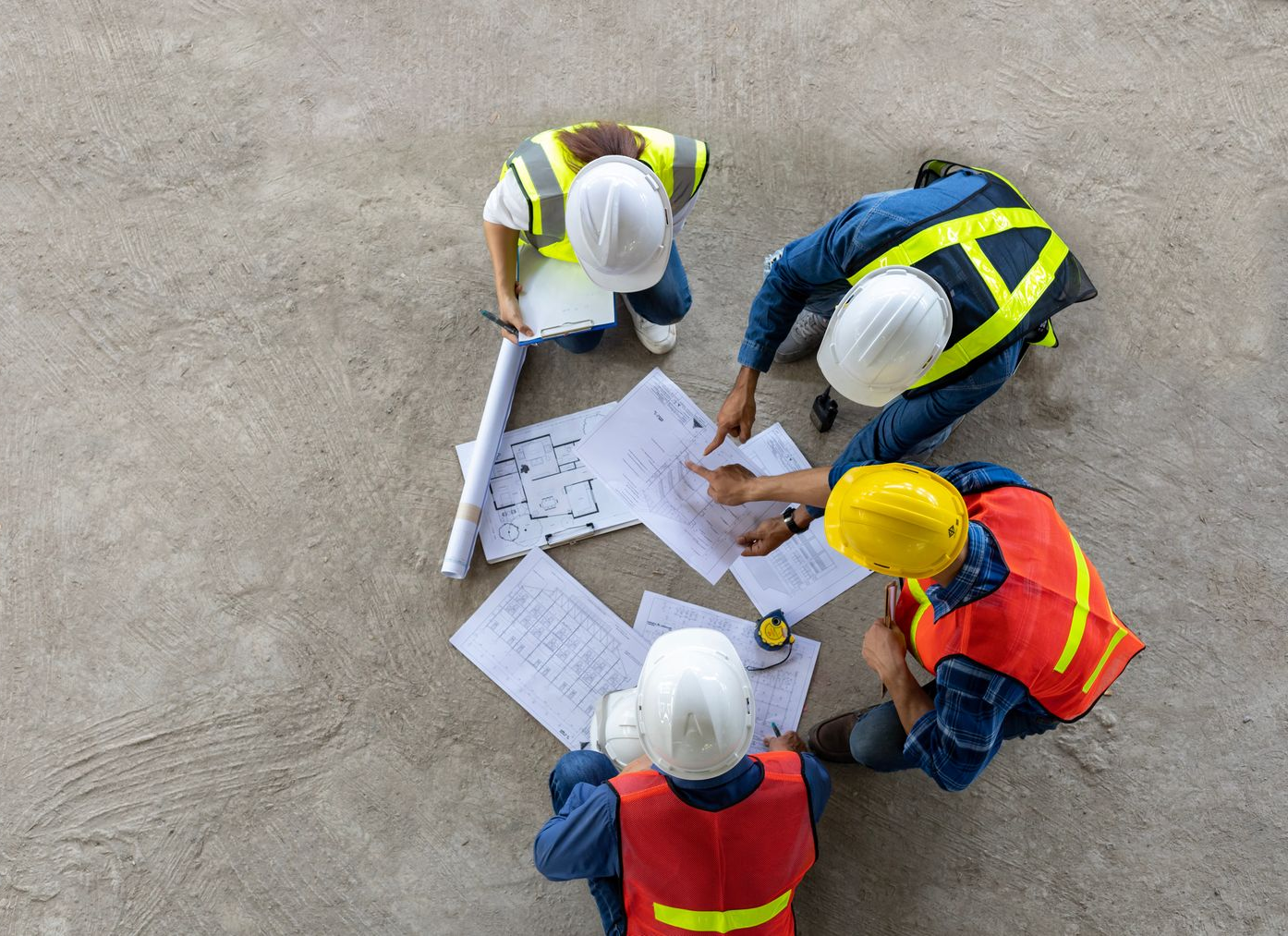 Woman in glasses smiles and points to a laptop while speaking to a man at a table, near a window.