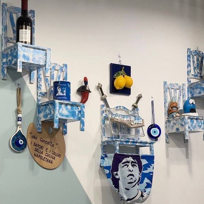 Mensole a forma di sedia dipinte di blu e bianco su una parete che espone oggetti decorativi, tra cui vino e opere d'arte.