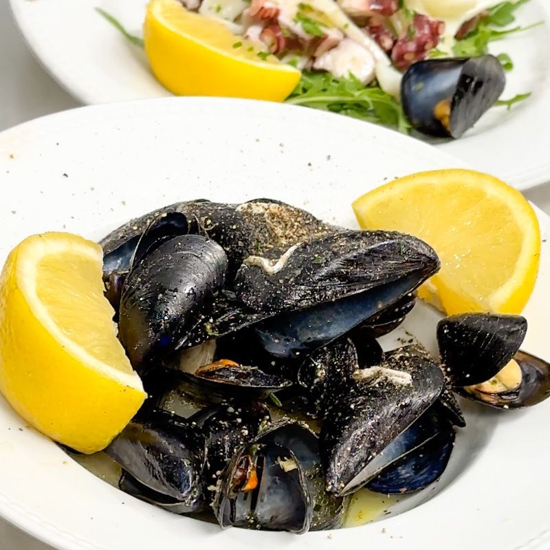 Piatto di cozze cotte con spicchi di limone. Un altro piatto sullo sfondo.