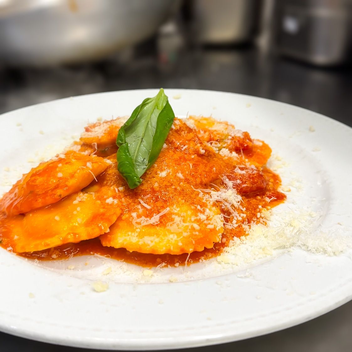 Ravioli al sugo di pomodoro, guarniti con basilico e parmigiano, su un piatto bianco.