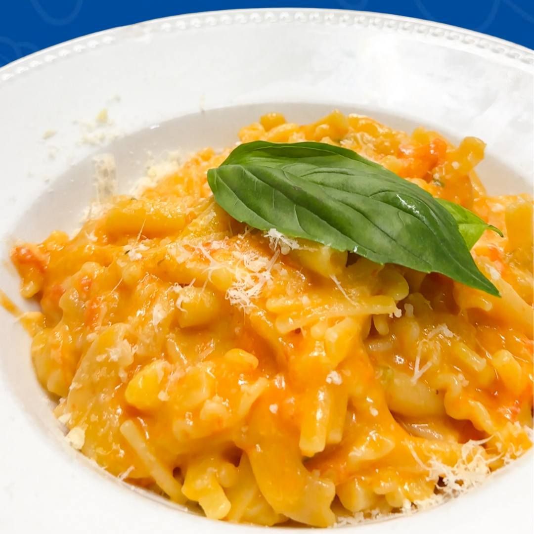 Piatto di pasta con salsa all'arancia, guarnito con basilico e parmigiano.