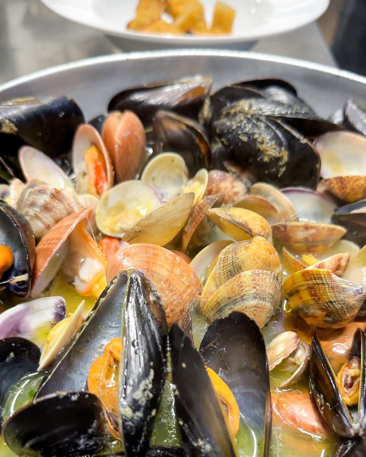 Primo piano di cozze e vongole in un brodo giallo. Alcune conchiglie sono aperte, rivelando la polpa arancione.