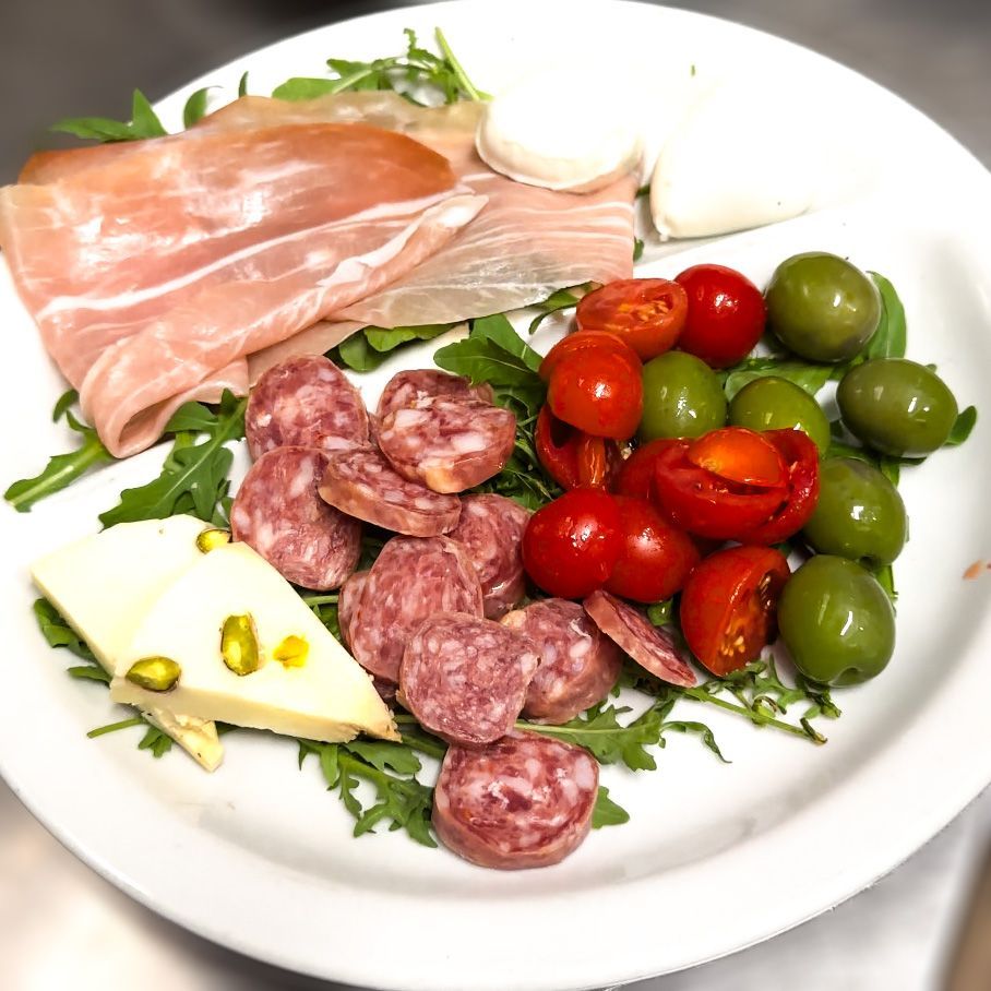 Piatto di antipasto con prosciutto, salame, mozzarella, pomodori, olive e formaggio.