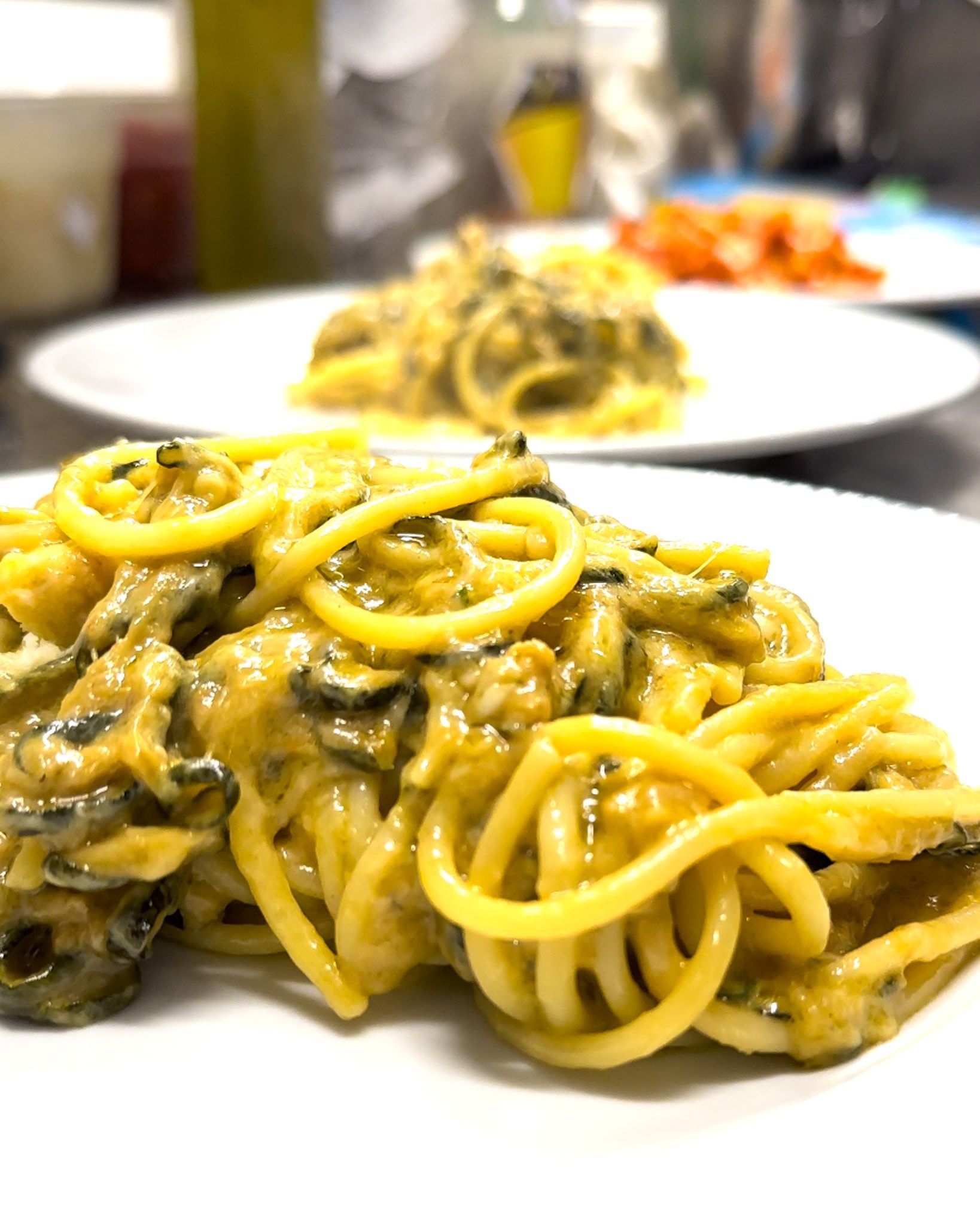Piatto di pasta con salsa gialla cremosa e verdure verdi, servito su un piatto bianco.