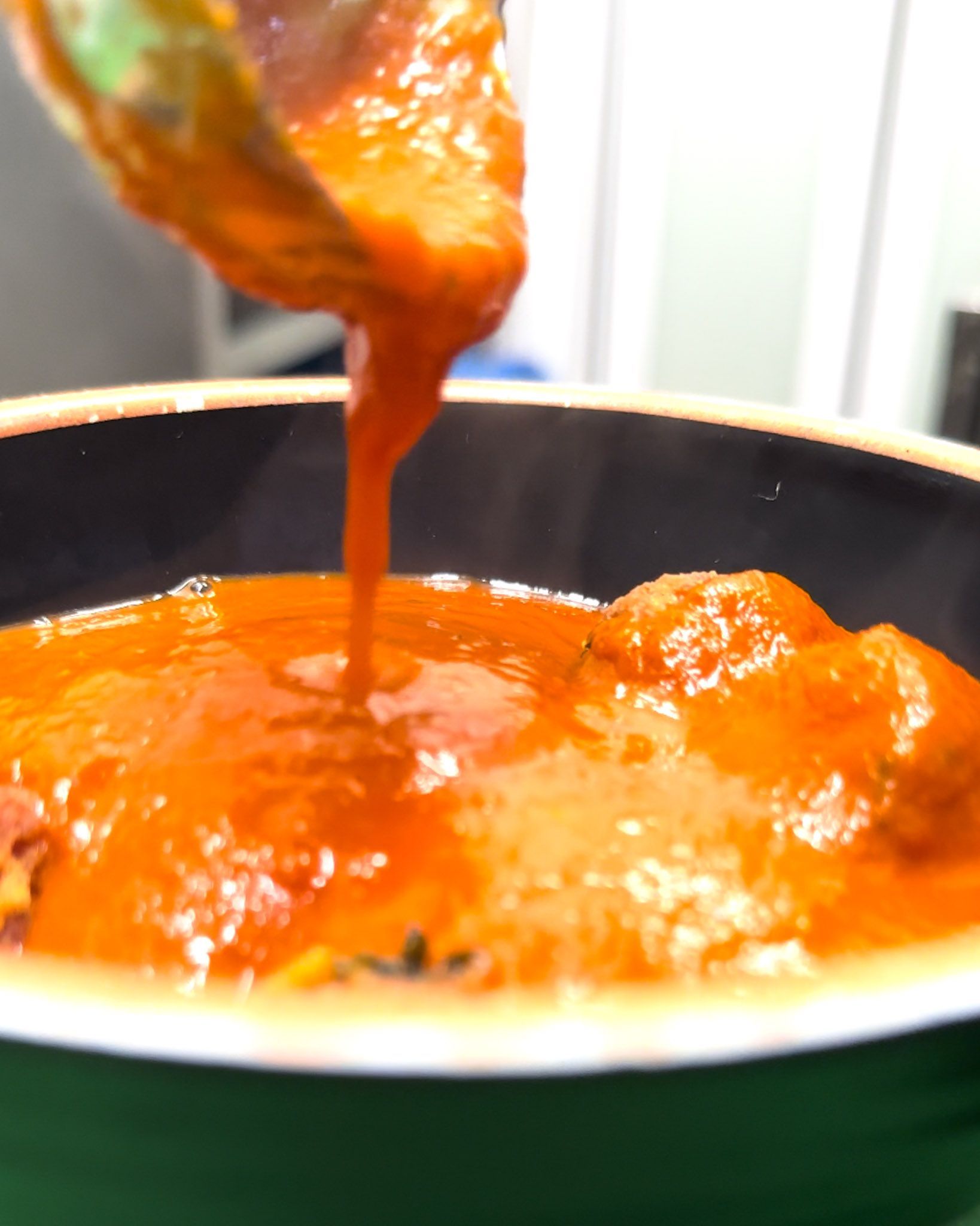 Salsa di pomodoro versata da un mestolo in una pentola verde, leggermente fumante.