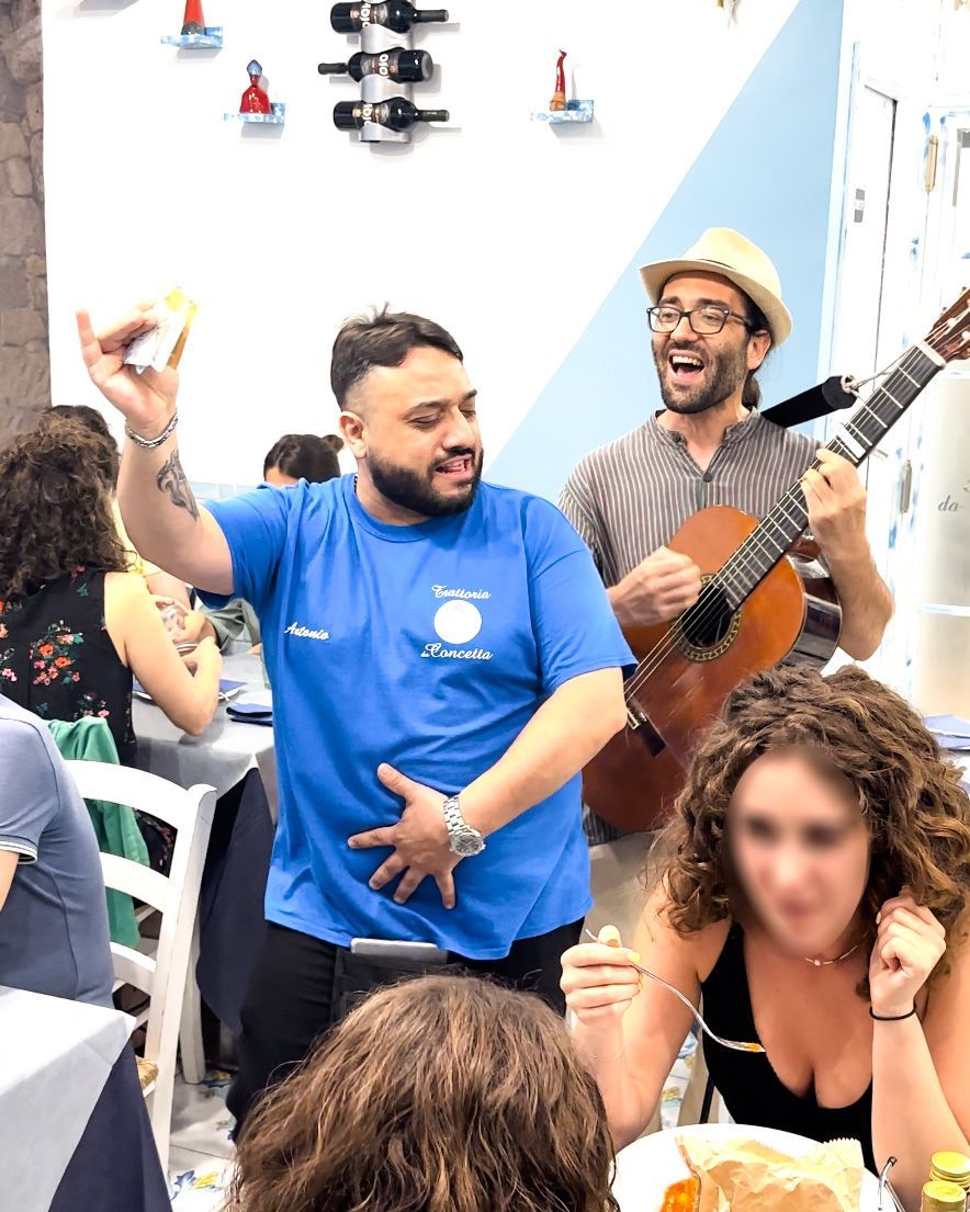 Un musicista suona la chitarra mentre un cameriere balla e tiene in mano un limone in un ristorante.