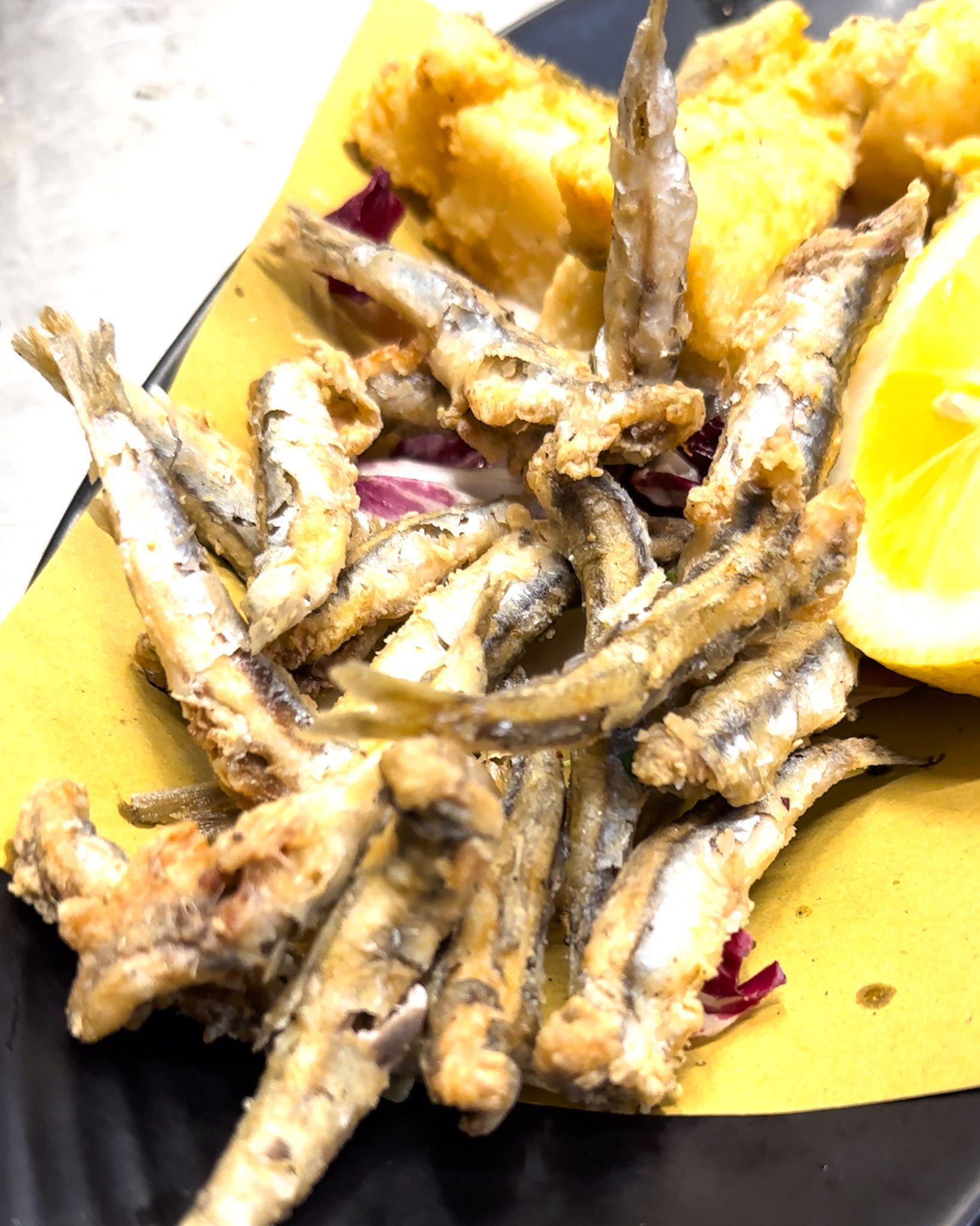 Pesciolini fritti e polenta, serviti con spicchi di limone su carta gialla.