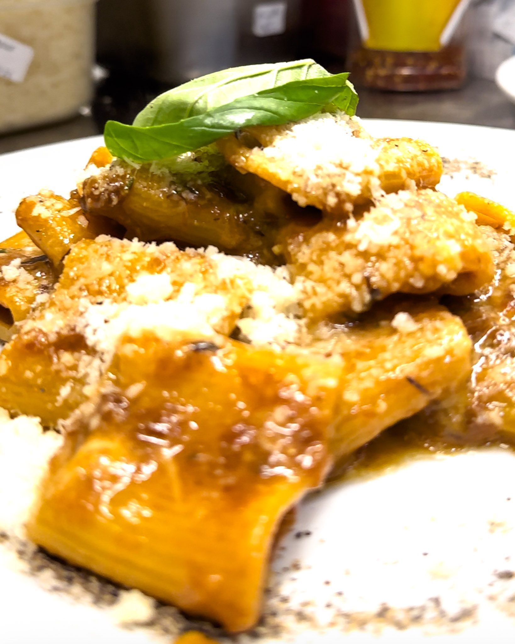 Piatto di pasta con sugo, formaggio grattugiato e guarnizione di foglie di basilico su un piatto bianco.