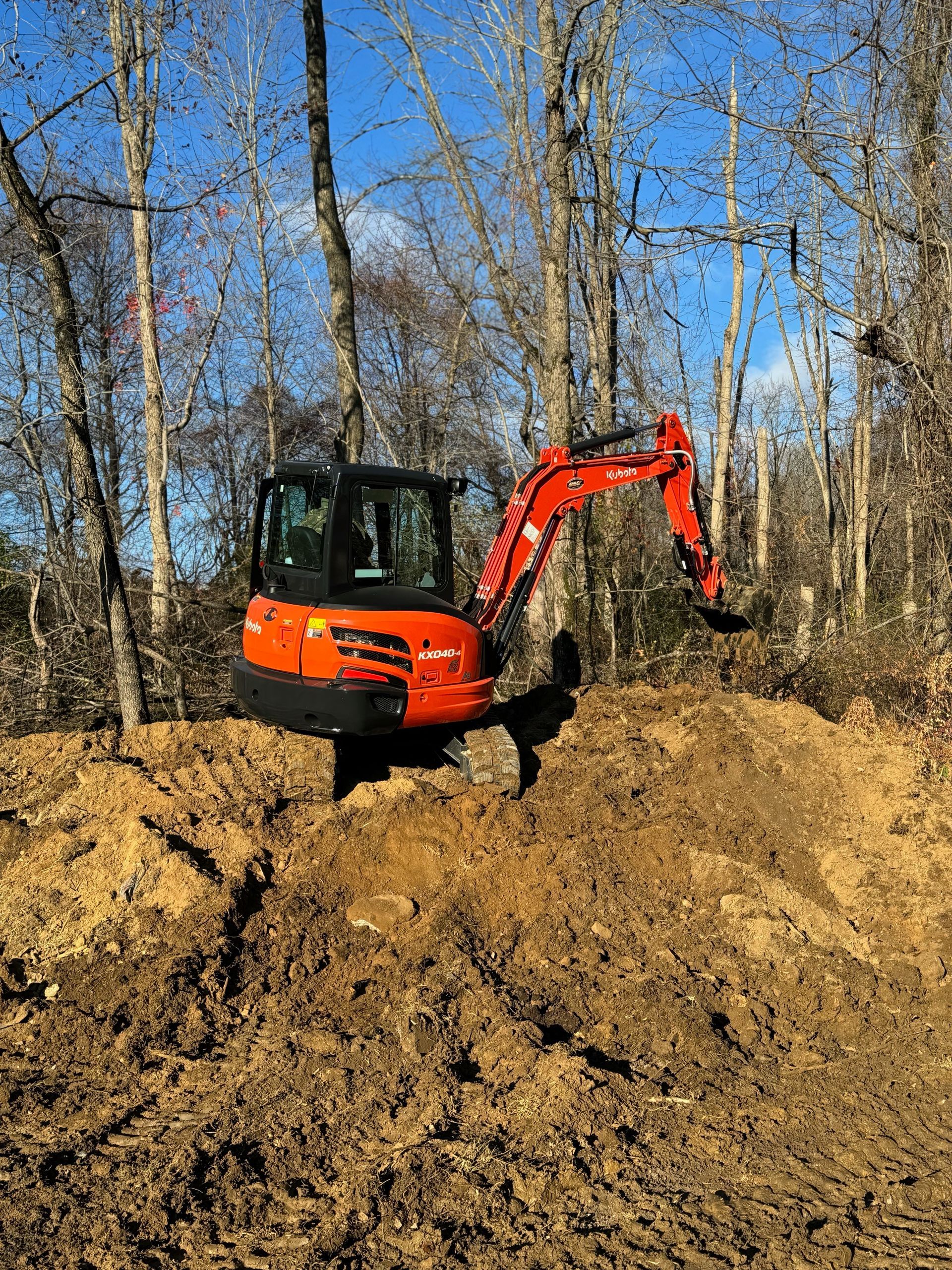 An orange excavator is digging a hole in the dirt in the woods.