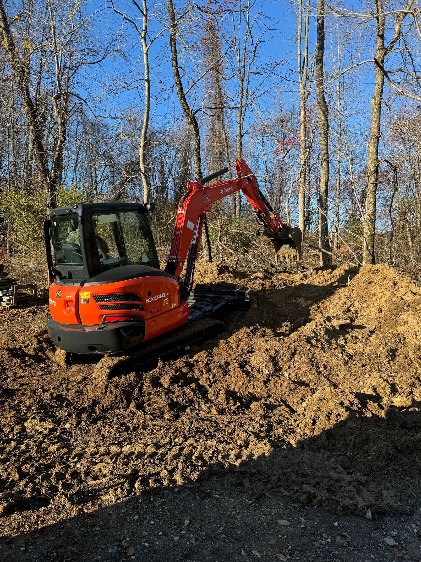 An orange excavator is digging a hole in the dirt in the woods.