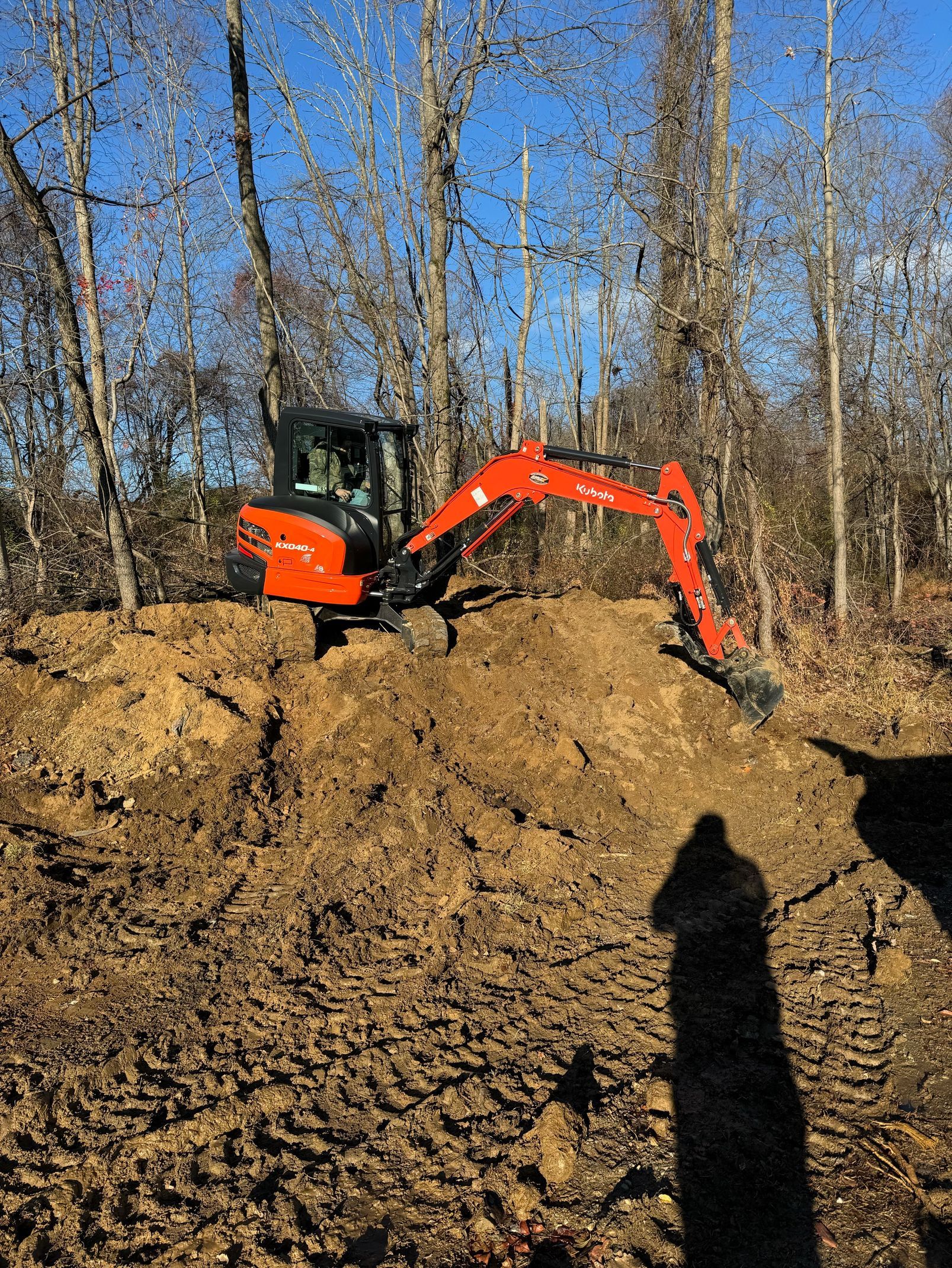 An orange excavator is digging a hole in the dirt in the woods.