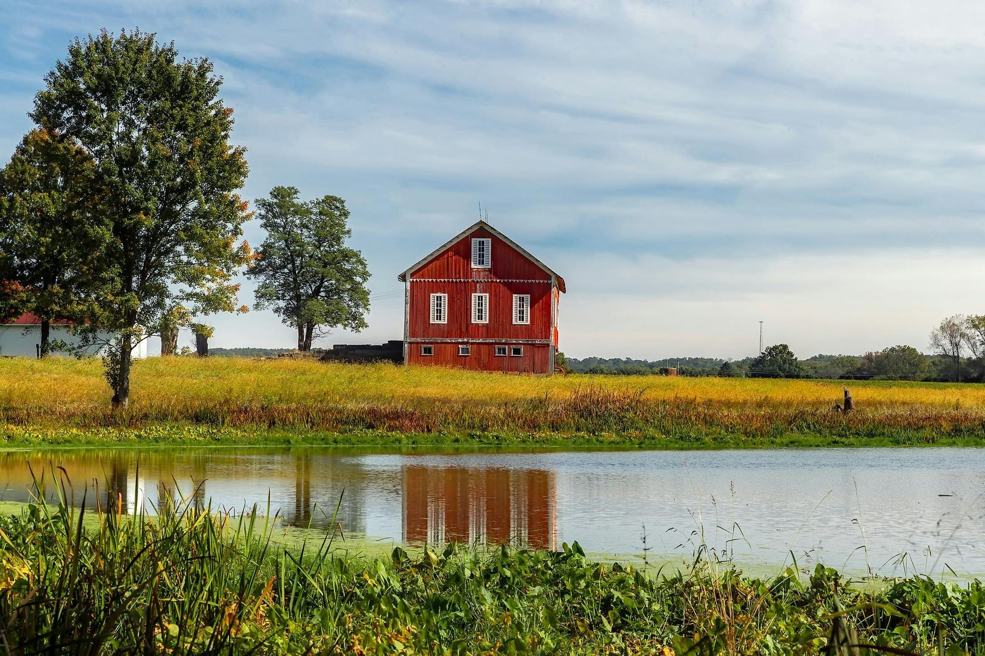 A red barn sits in the middle of a field next to a pond.