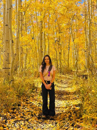 Woman stands on a path in a forest of yellow fall foliage.