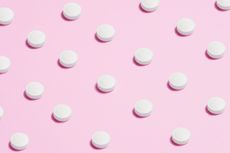 White pills arranged on a pink background, evenly spaced, casting shadows.