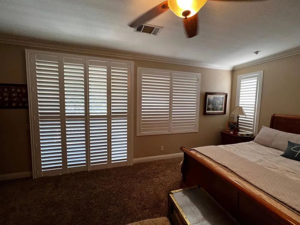 Bedroom with white shutters on windows, brown carpet, and a wooden bed.