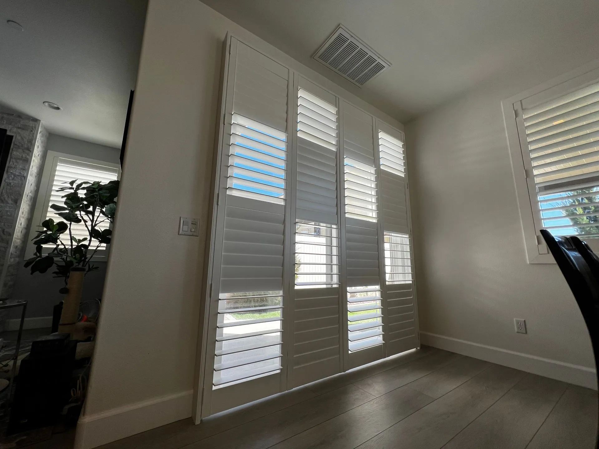 Interior room with white shutters, a window, and light wooden floor.